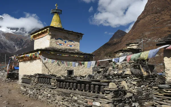 A weathered stone chorten with painted Buddha Eyes gazing out over snowy peaks
