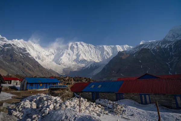 Red and blue lodge roofs below the snow-covered wall of the Annapurna Sanctuary