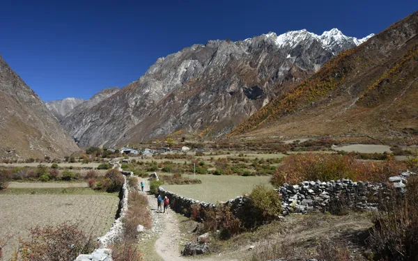 Trekkers walking between stone walls toward a settlement