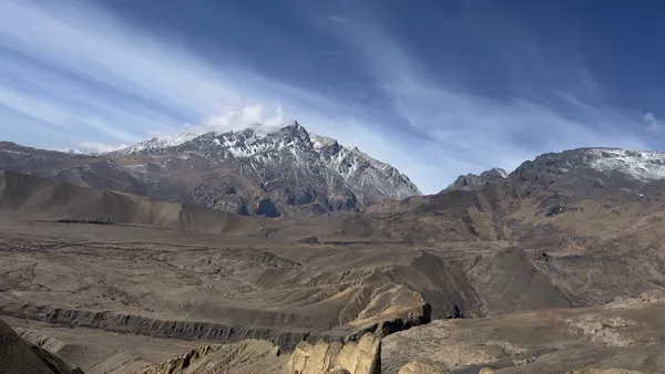 Vast brown landscapes and sharp ridges leading toward a solitary jagged peak under wispy skies