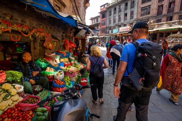 Tourists walking past a local vendor in a narrow Kathmandu alley