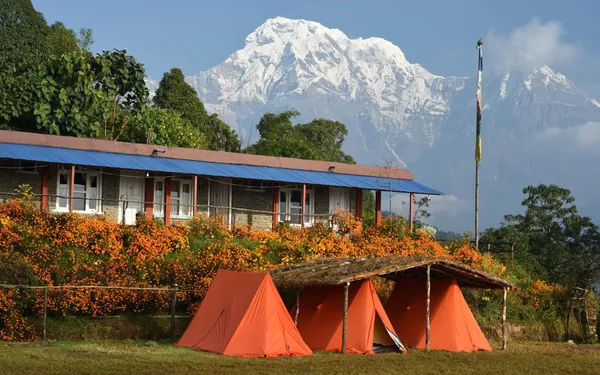 Orange trekking tents and a mountain lodge beneath Annapurna South