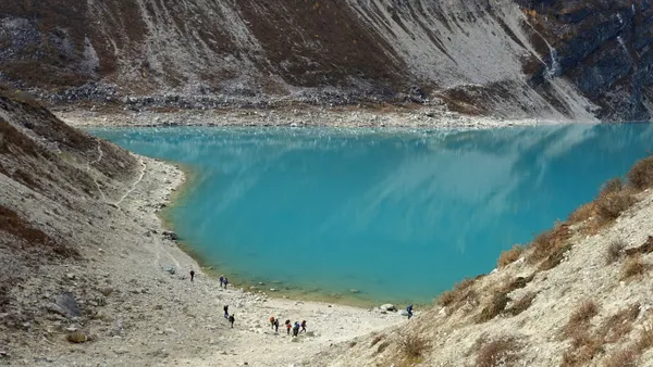 Trekkers walking along the turquoise glacial waters of Birendra Lake beneath towering slopes