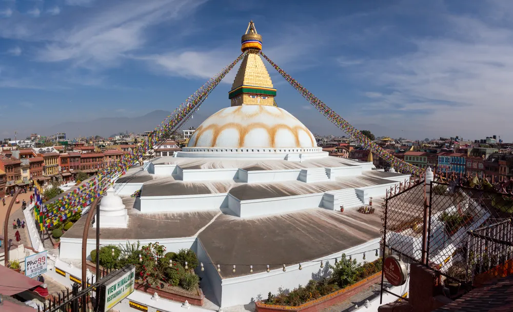 The white dome and golden spire of Boudhanath Stupa surrounded by colourful prayer flags