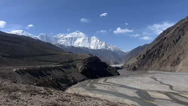 Wide braided riverbeds winding through high-altitude desert canyons toward Himalayan peaks