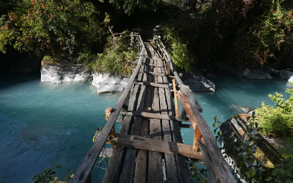 A wooden bridge spanning a turquoise mountain stream