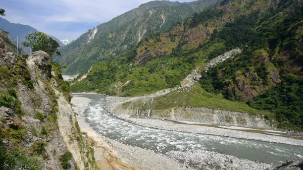 The trail following the wide Budi Gandaki River through a valley of towering green mountains