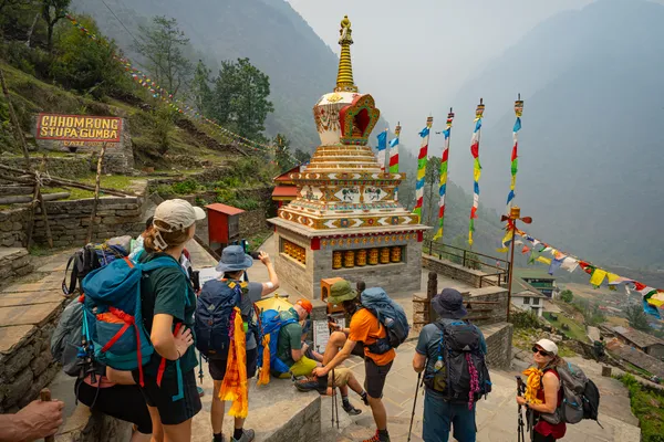 Trekkers passing a colorful Buddhist stupa and prayer flags in Chhomrong