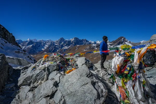 A trekker by prayer flags at 5,420 m gazing toward the Himalayan horizon