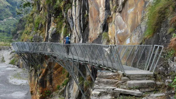 A trekker traversing a metal walkway bolted into a cliff