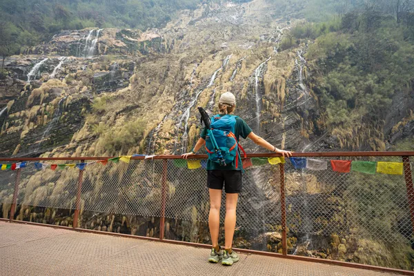 A trekker looking up at waterfalls cascading down a broad rock face