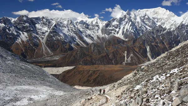 Two hikers descending a steep trail with the vast mountain range stretching before them