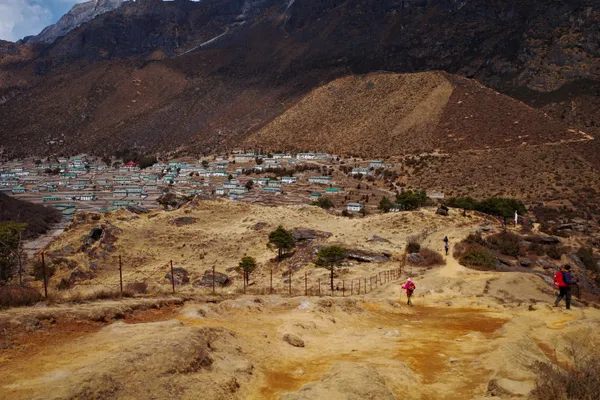 Trekkers follow the dusty trail toward the green-roofed houses of Khumjung