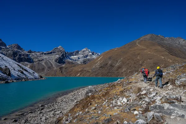 Porters and trekkers follow the lakeside path heading south toward Machhermo