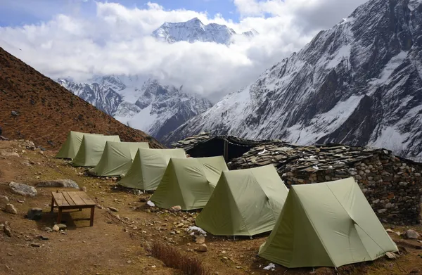 A row of green tents and stone shelters at the high camp beneath snowy peaks