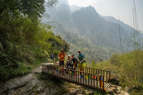 Hikers on a small metal footbridge surrounded by forest and steep cliffs