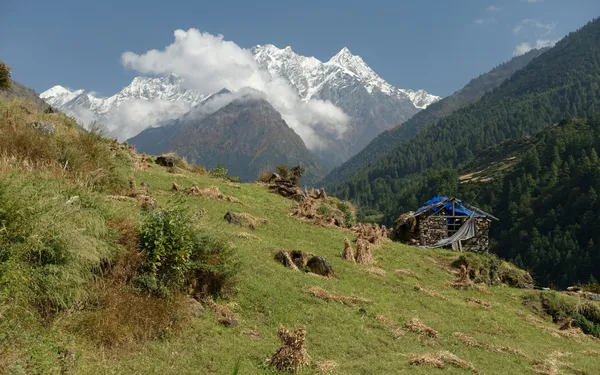A stone shelter on a green hill with Ganesh Himal beyond