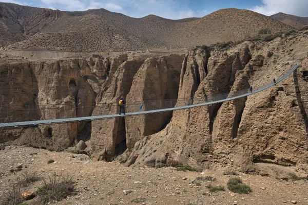 Trekkers crossing a long suspension bridge spanning a deep erosion-carved river gorge