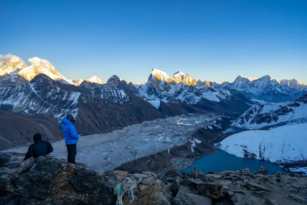 Trekkers gazing down at turquoise Gokyo Lake and village from the peak