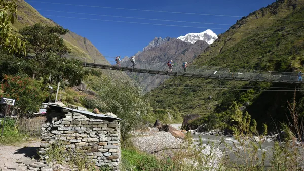 Trekkers crossing a long suspension bridge with mountains beyond