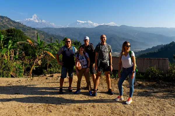 A group of trekkers posing on a sunny path with the Himalayas behind them