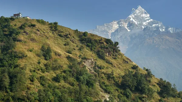 A small guesthouse perched on a green hilltop with Machhapuchhre behind