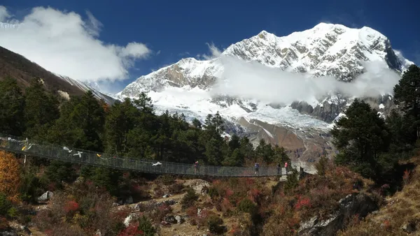 Hikers crossing a long suspension bridge with white glaciers in view