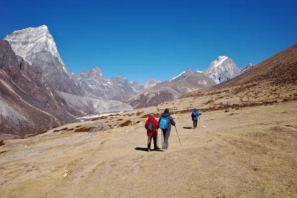 Hikers traversing the wide glacial valley beneath towering Taboche peak