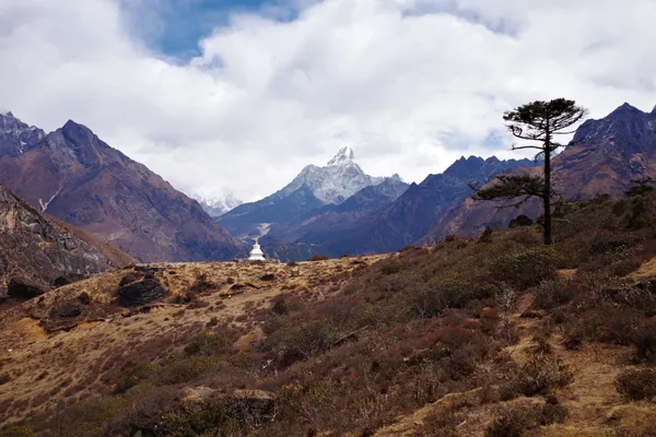 A solitary tree and a distant stupa frame mountain peaks along the trail to Khumjung