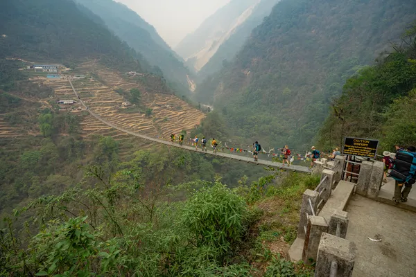 Trekkers crossing a long suspension bridge above a deep terraced valley