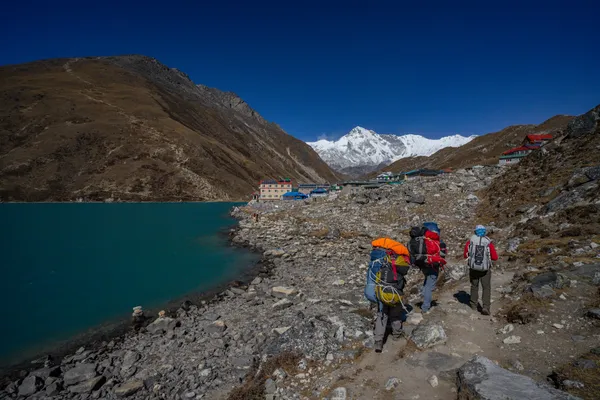Trekkers follow the lakeside path toward Gokyo village with snow-capped peaks