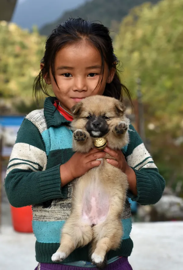 A young girl from a mountain village smiling while cradling her fluffy puppy