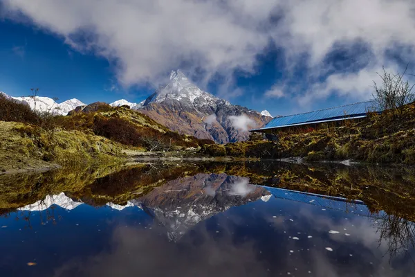 Machhapuchhre and passing clouds reflected in a small pond beside a lodge