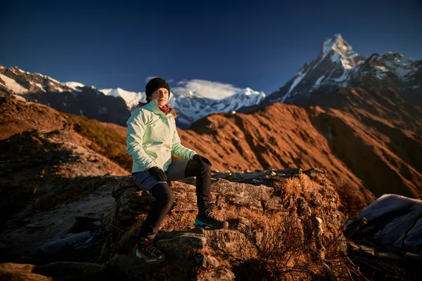 A trekker sitting on a rock beside golden ridges with Machhapuchhre beyond