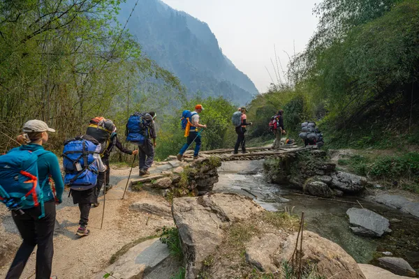 Hikers crossing a small stone-slab footbridge over a mountain stream