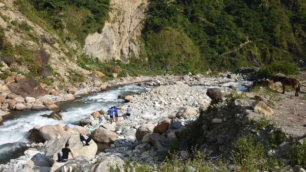 Pack mules and trekkers resting on a rocky riverbank