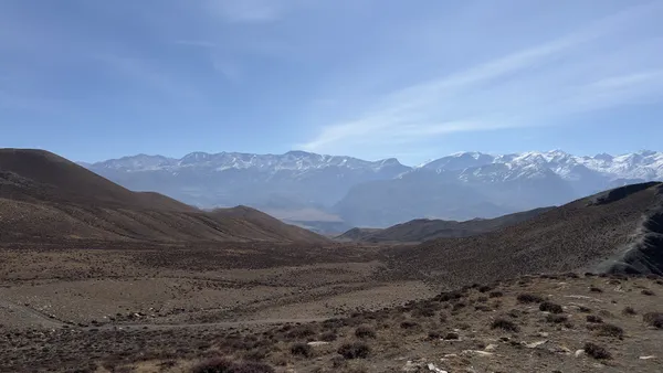 Rolling arid hills stretching toward a jagged horizon of distant snow mountains