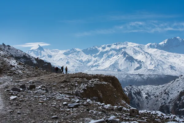 Trekkers pausing to admire a vast snow-capped mountain range under a clear blue sky on the ascent to Yamda La
