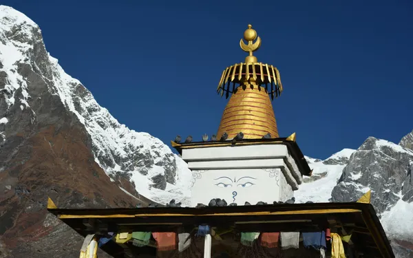 A golden Buddhist stupa with Buddha eyes and prayer flags beneath snow-capped peaks
