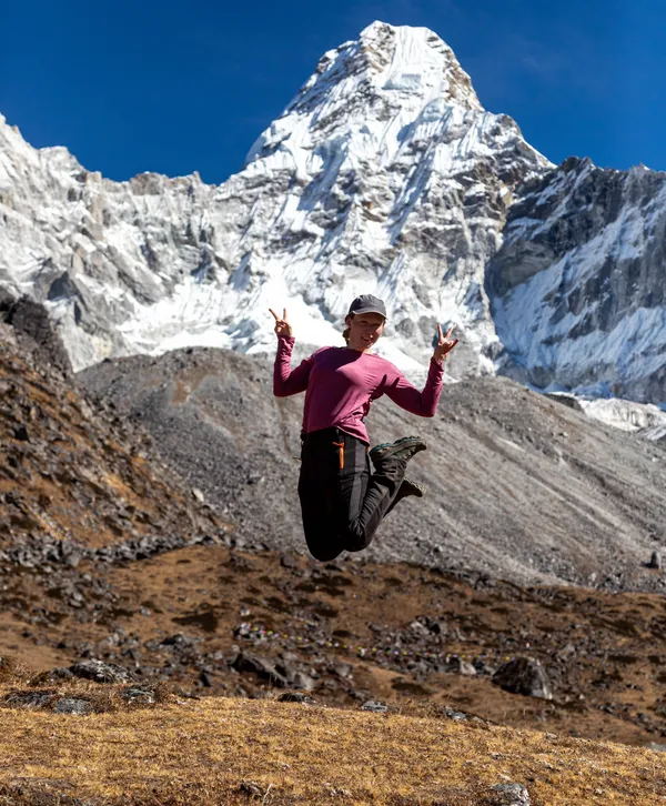 A trekker jumping for joy in front of Ama Dablam