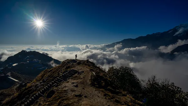 A silhouetted trekker standing at the end of a stone-stepped ridge above the clouds