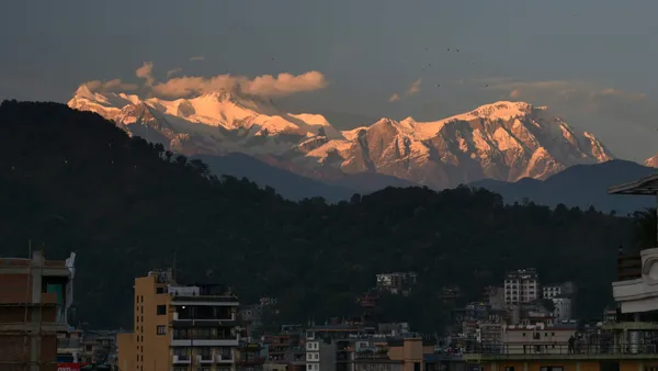 Pink and gold light on Himalayan peaks above wooded hills and Pokhara buildings