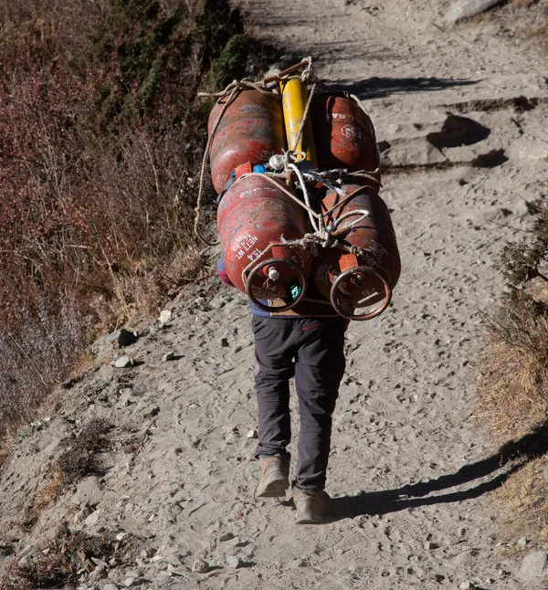 A local porter hauling four red gas cylinders up the rocky trail
