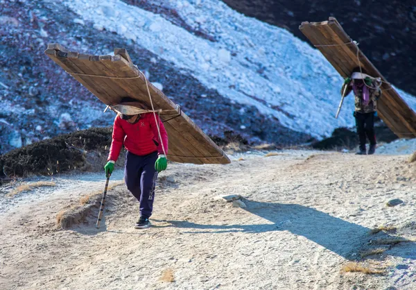 Local porters carrying heavy timber planks uphill near Lunden