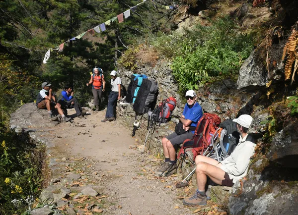 Trekkers resting beside colorful prayer flags on a hillside