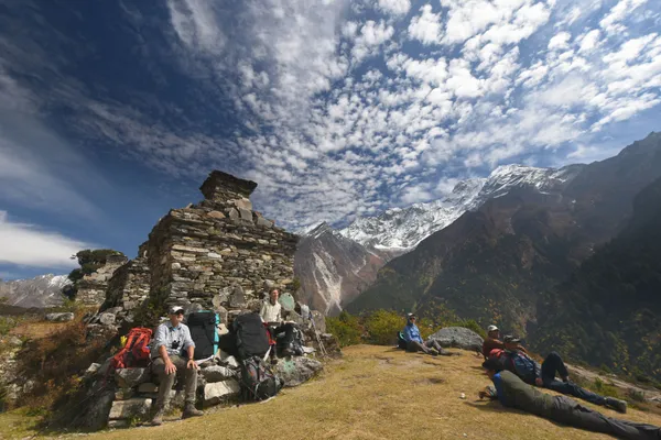 Trekkers pausing near weathered stone chortens with mountains beyond