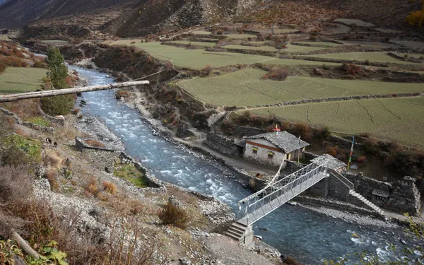 A metal bridge spanning a swift river beside green fields