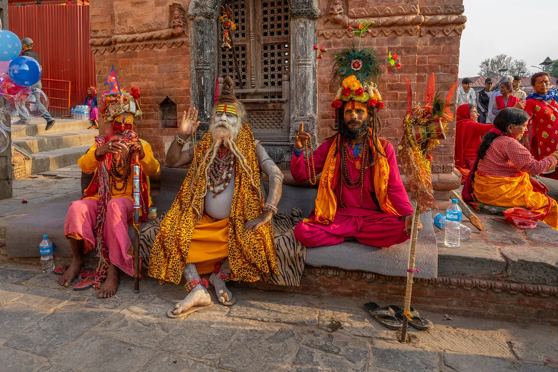 Three sadhus in colourful traditional clothing seated outside a brick shrine at Pashupatinath