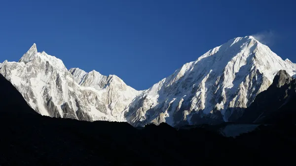Jagged snow-capped peaks gleaming in the sunlight against a deep blue sky