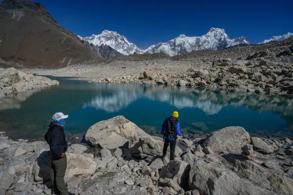 Trekkers at the edge of Fifth Lake with mountains reflecting in the water